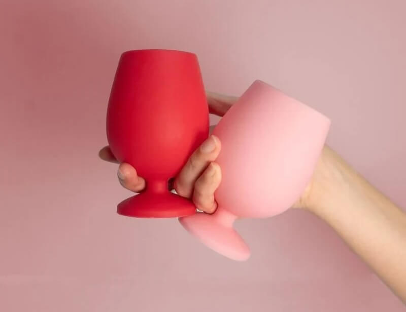 A person holding a red cup and a pink cup against a pink background.