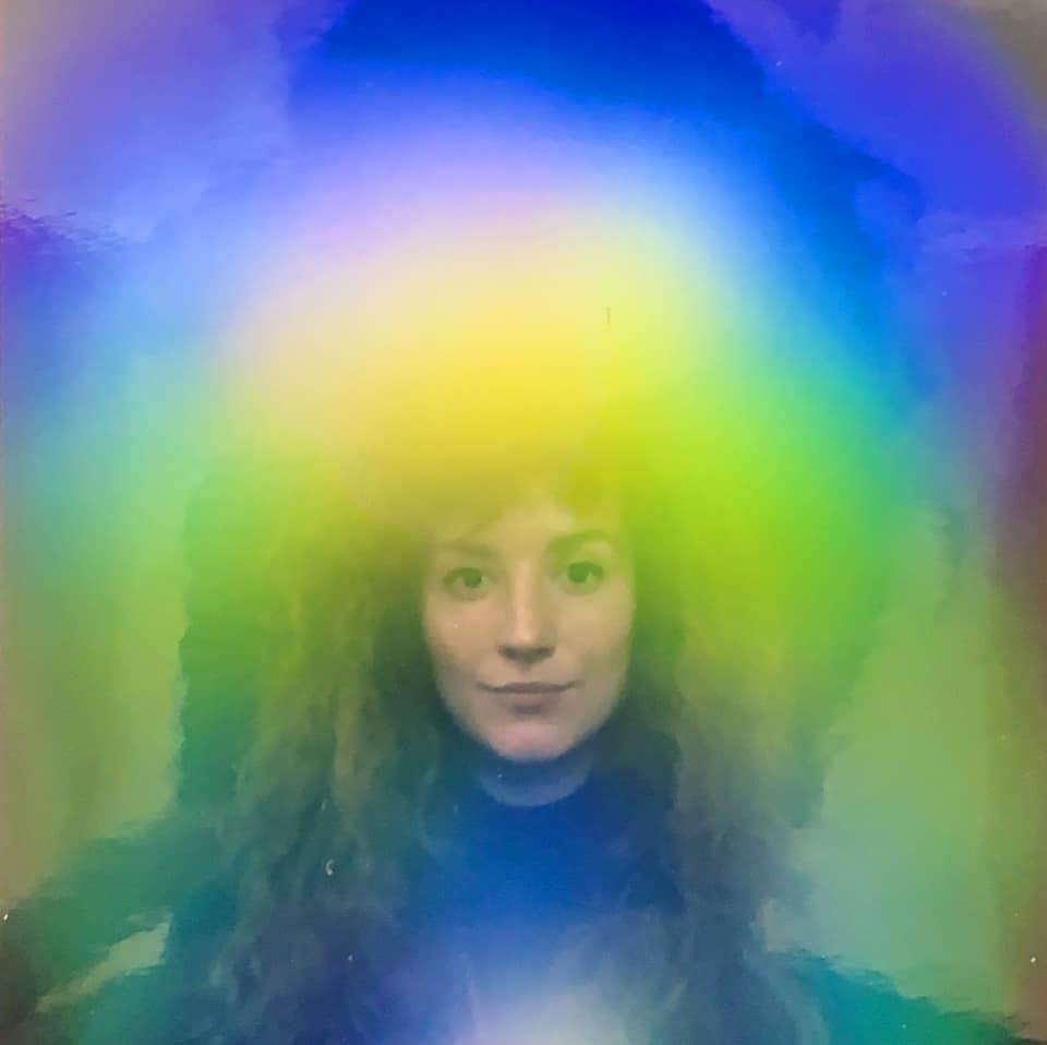 A person with long, curly hair is surrounded by a vibrant, multicolored aura with hues of blue, yellow, and green at a lively Nashville event.