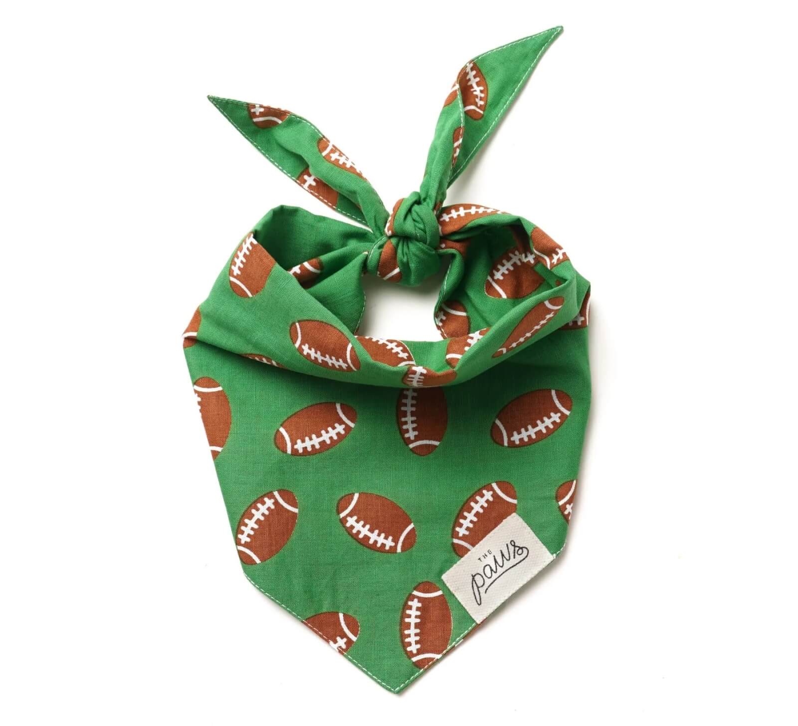 Green bandana with a football pattern and a label reading "Paws" in the bottom corner, tied into a knot. 