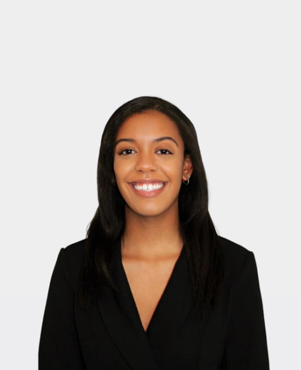 Alex Evelyn, a woman in a black blazer, is smiling radiantly against a plain white background.