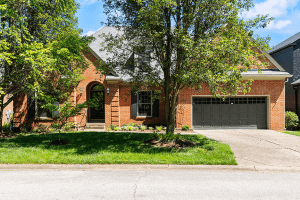A charming brick house with a grey garage door, nestled among trees and lush green lawn on Rivers Edge Road, Louisville KY, enjoying the warmth of a sunny day.