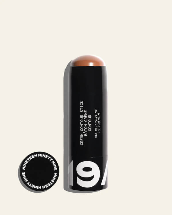 A black cream contour stick with the cap removed, displaying the brown makeup product. The cap lies beside it, labeled "Nineteen Ninety Nine.
