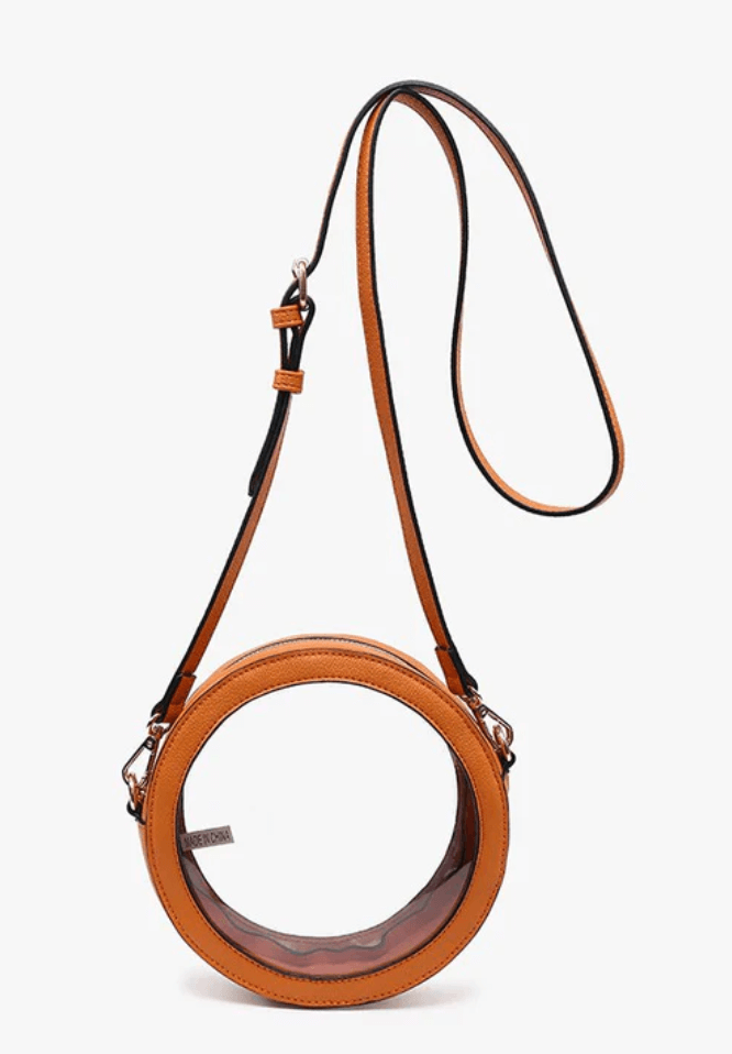 A circular, clear plastic handbag with tan leather trim and a long adjustable strap, displayed on a plain white background.