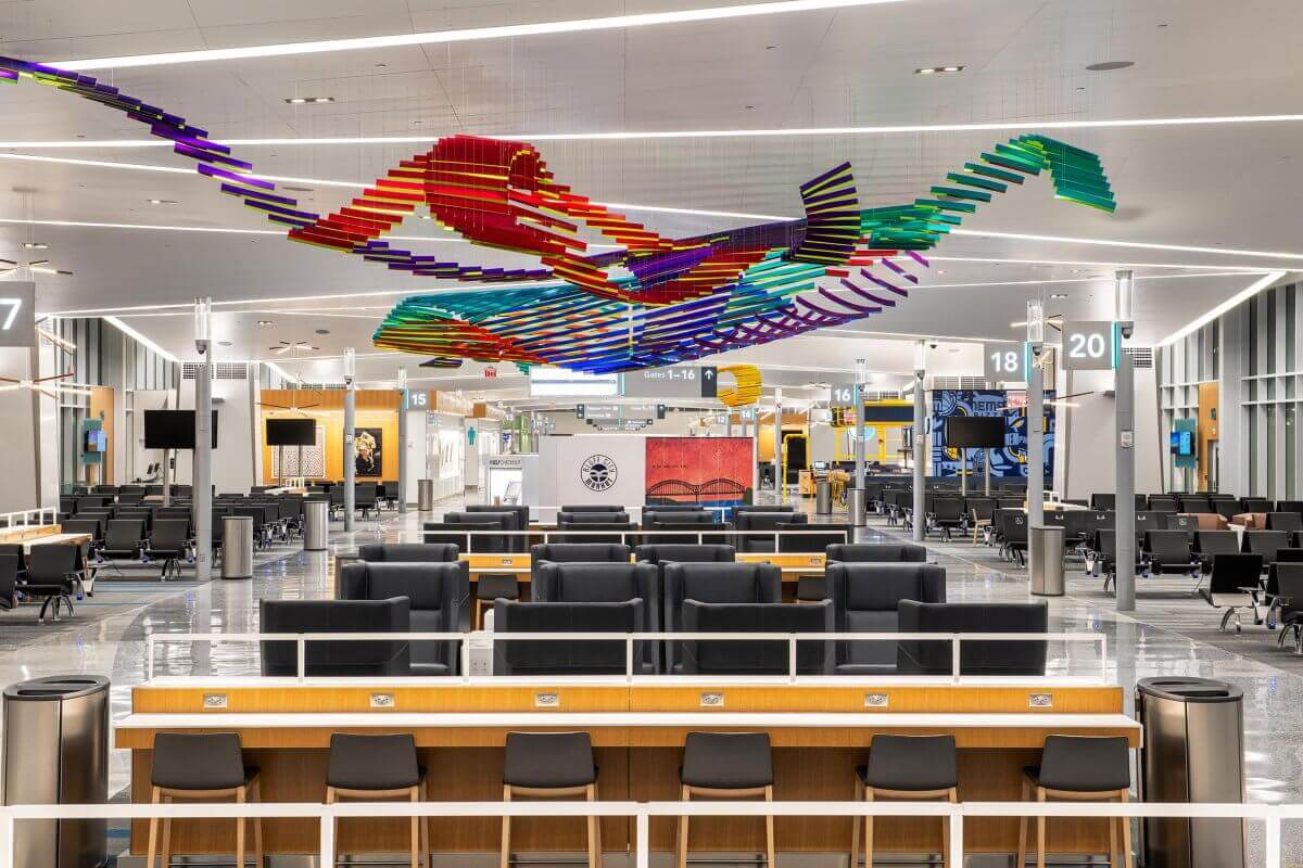 The modern airport terminal interior boasts comfortable seating, digital screens displaying direct flights from Memphis, and a colorful abstract ceiling sculpture.