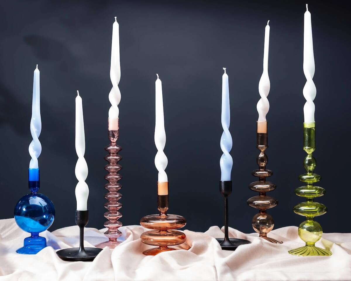 18 Nashville FINDS for Late Summer: Jewelry, Decor & More - 3 Six white twisted candles in glass holders of varying shapes and colors, arranged on a draped light fabric against a dark background—a chic accent featured in Nashville August FINDS.