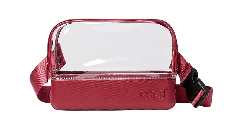 A maroon crossbody bag blends style with function, featuring a clear bag-inspired transparent upper half, solid bottom, adjustable strap, and buckle closure. The word "bogg" is embossed on the lower section.