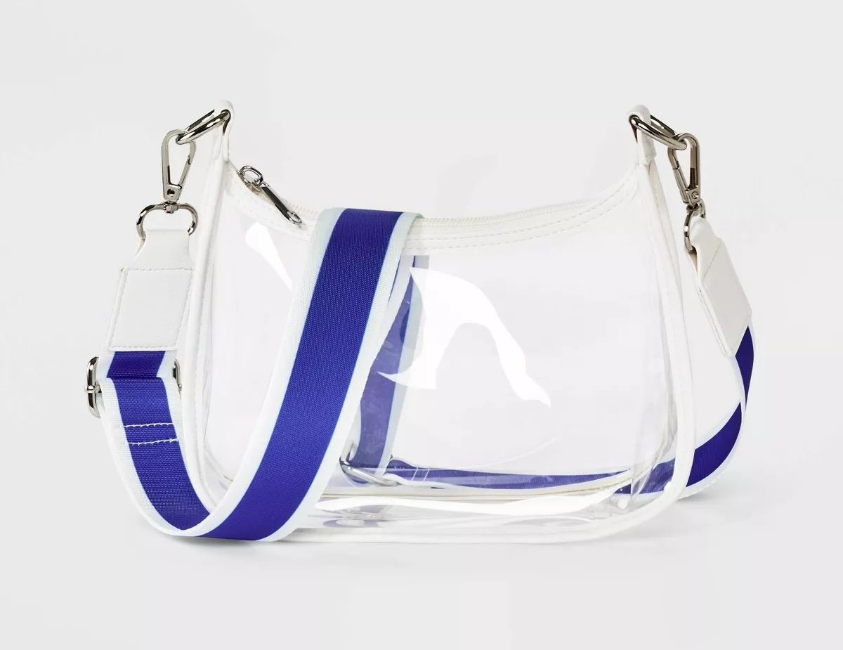 A stylish clear bag, this plastic crossbody features a white zipper and a detachable white and blue striped strap, all set against a plain light background.