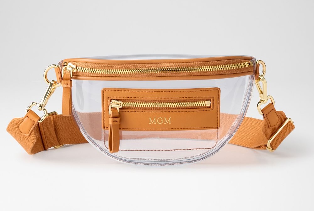 Clear plastic belt bag with tan leather trim, gold zipper, front pocket, adjustable strap, and "MGM" initials on the front—an on-trend choice for clear bags lovers.