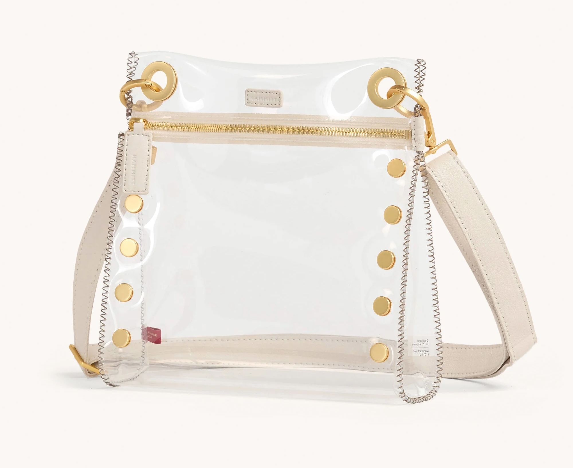 A clear, rectangular handbag with gold hardware, beige strap, gold snaps, and a zippered closure—a chic addition to your collection of clear bags.