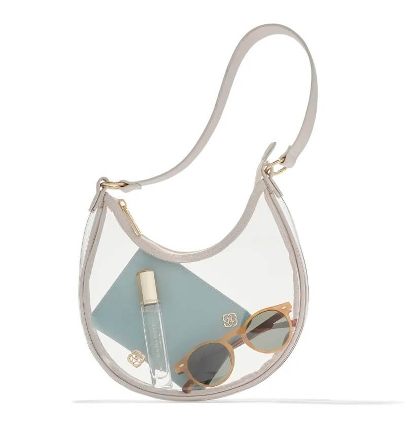 A clear bag with a white strap contains sunglasses, a small perfume bottle, a light blue wallet, and a pair of stud earrings.