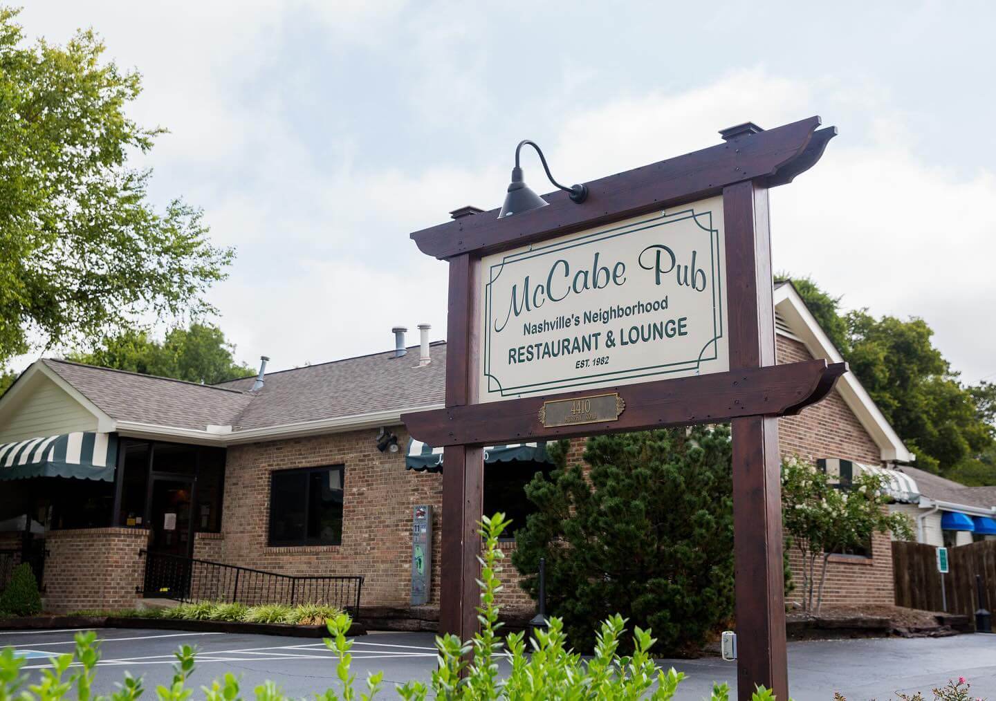 A wooden sign reads "McCabe Pub - Nashville's Neighborhood Restaurant & Lounge - EST. 1982" in front of a brick building with a striped awning and greenery, standing resilient amid recent restaurant closures in the ever-changing industry.