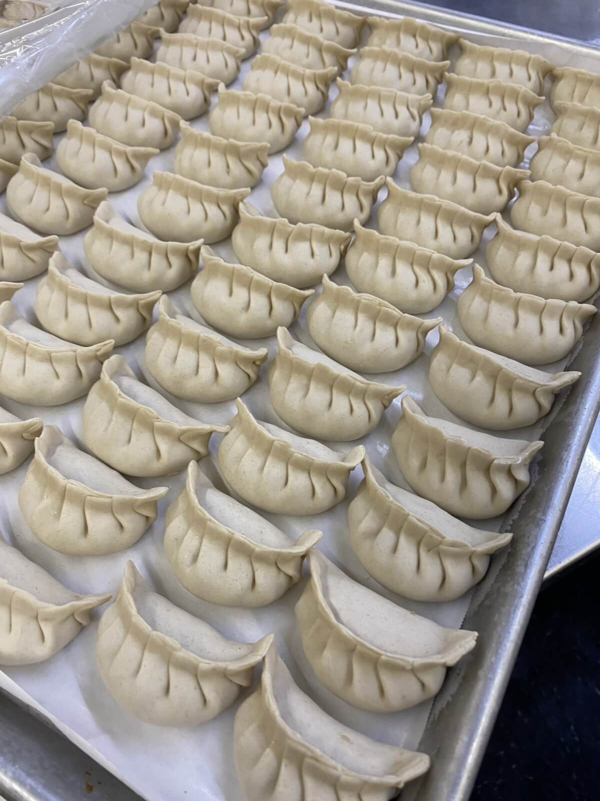 A tray filled with neatly arranged, uncooked dumplings lined up in rows on parchment paper, reminiscent of the meticulous care and tradition passed down from MAMA YANG.