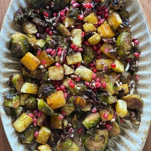 A platter of maple-glazed Brussels sprouts and diced potatoes topped with pomegranate seeds.