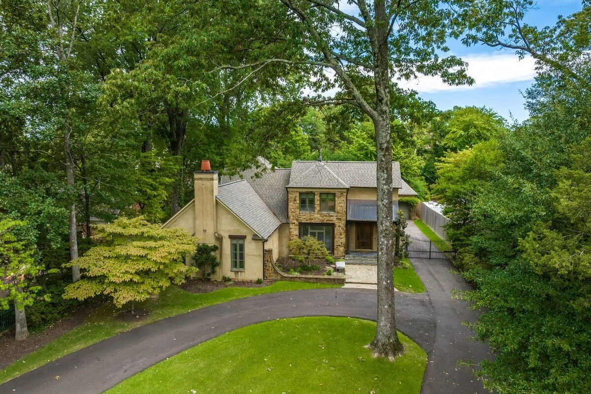 A two-story house with a mix of stone and stucco exterior, surrounded by trees, featuring a curved driveway and a side gate located in Memphis, TN on Tuckahoe Rd.