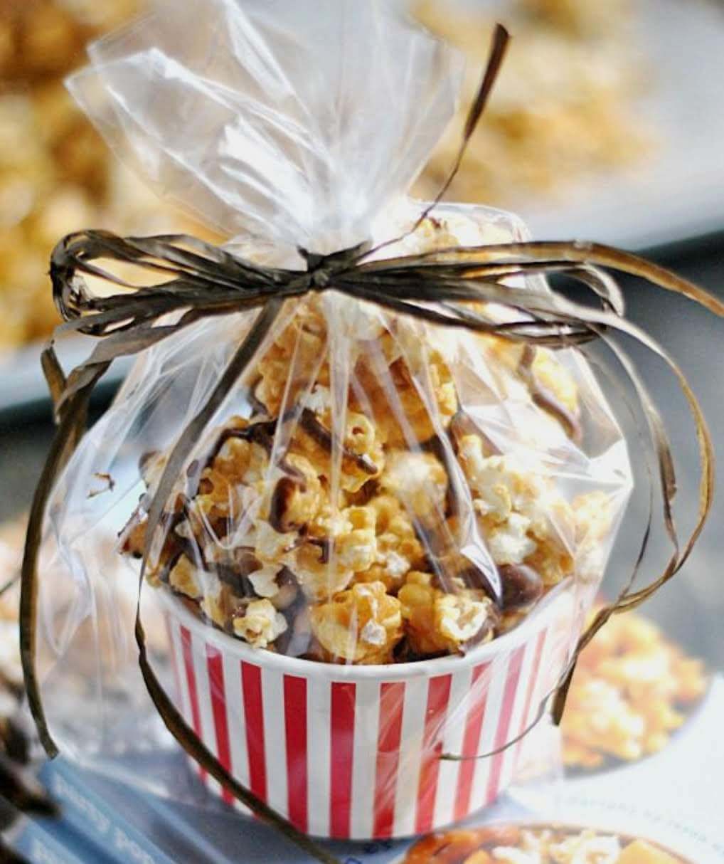 A red and white striped cup filled with Pop's Kernel caramel popcorn is wrapped in clear plastic tied with a brown ribbon.