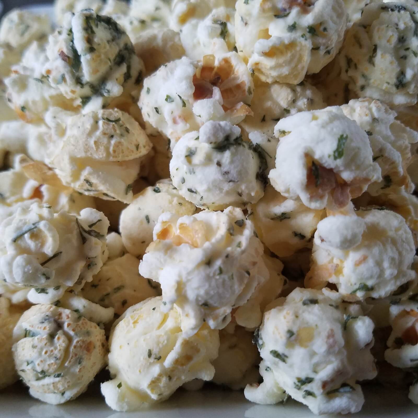 Close-up image of a pile of Pop's Kernel popcorn, seasoned to perfection with visible bits of herbs and spices.