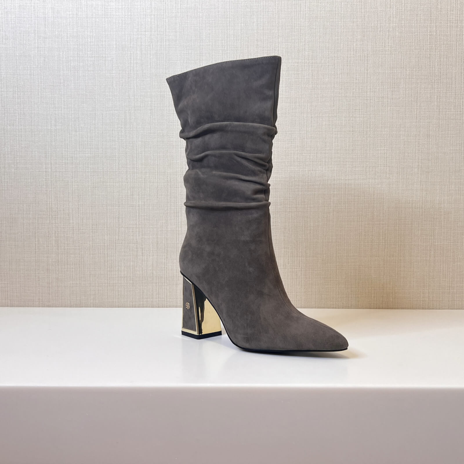 A single gray suede high-heeled boot with a slouchy design and a gold-accented block heel displayed on a white surface.