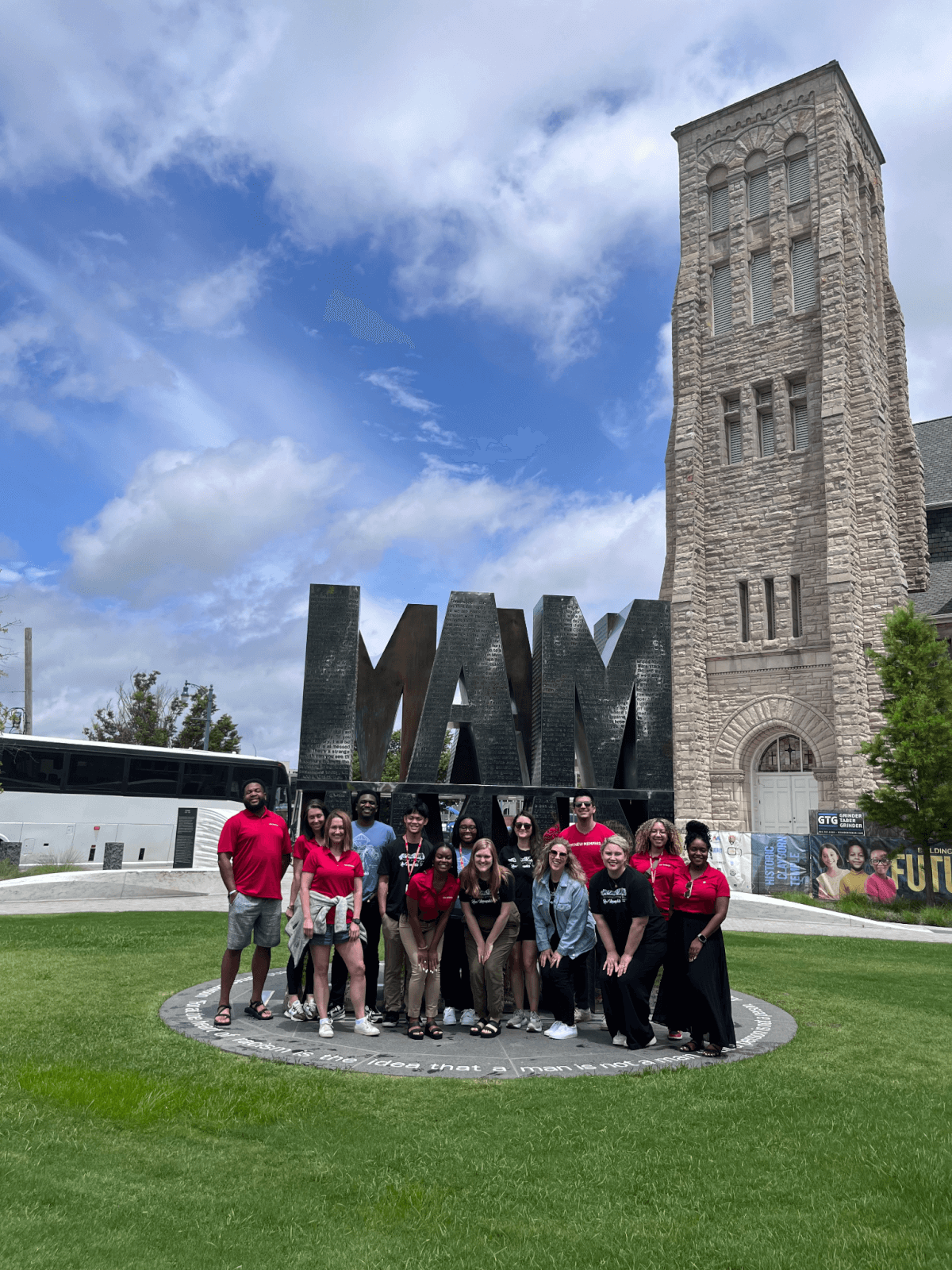 A group of people stands in front of the large "I AM A MAN" monument, set against the backdrop of a stone building, beautifully spotlighting the spirit of New Memphis.