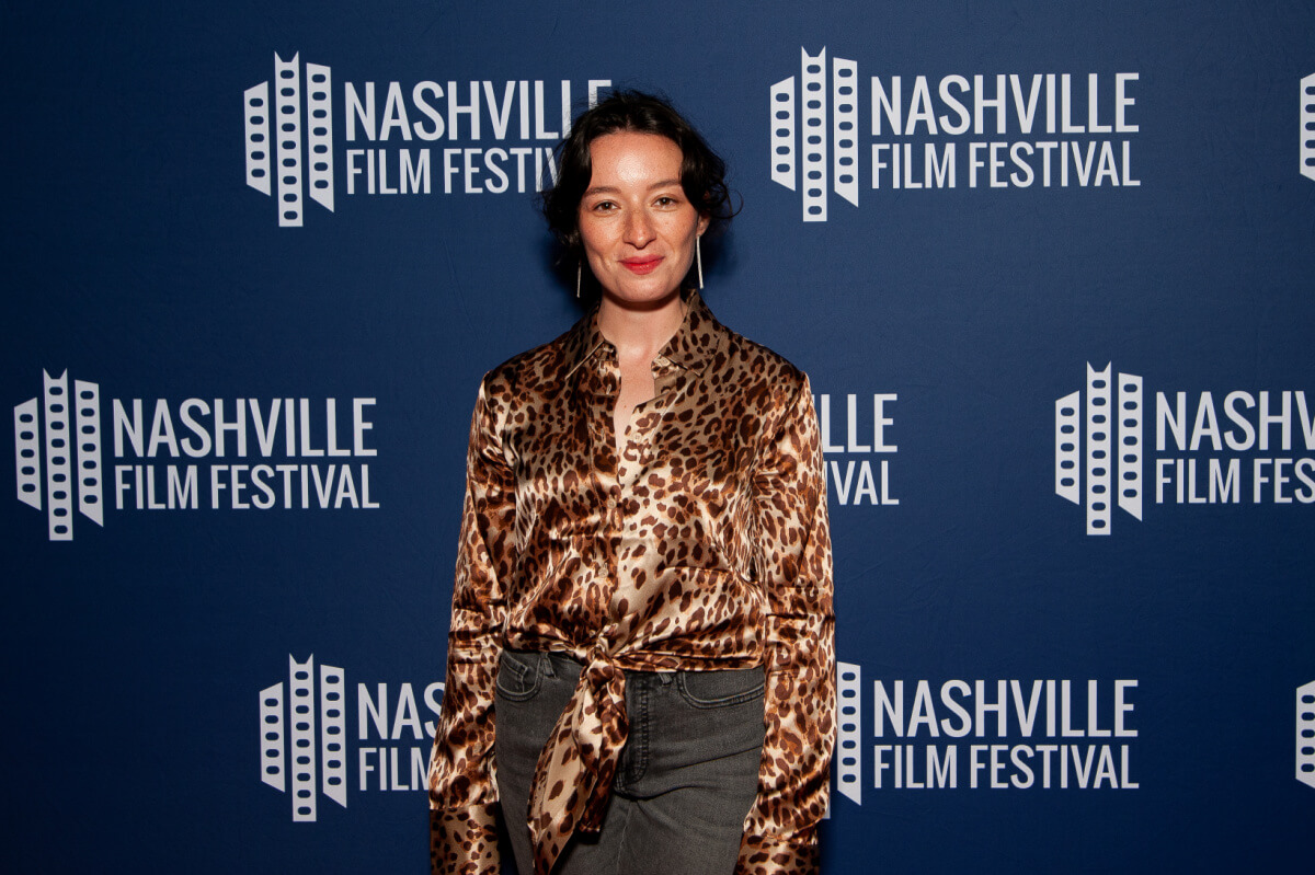 A woman in a leopard print blouse stands in front of a backdrop adorned with "Nashville Film Festival" logos.
