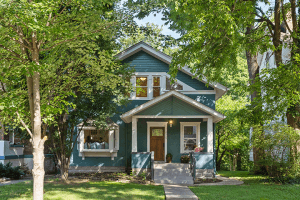 Tucked away on Kenilworth Place in Louisville, KY, this two-story green house features a charming wooden front door and a cozy porch, all enveloped by lush green trees and a manicured lawn.