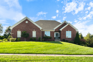 Nestled in Crestwood KY, this red brick house on Northwind Court features a large lawn under a blue sky with clouds.