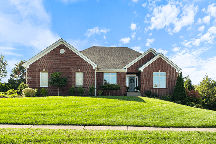 Nestled in Crestwood KY, this red brick house on Northwind Court features a large lawn under a blue sky with clouds.