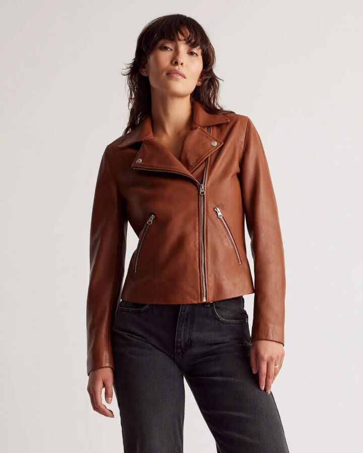 A person wearing a stylish brown leather fall jacket and black pants stands against a plain background.