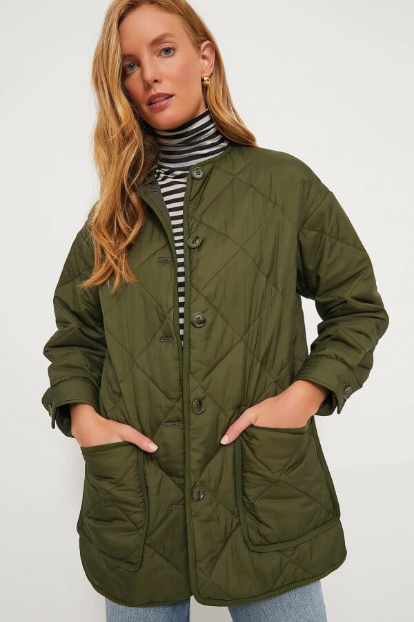 A person wearing a chic green quilted coat, one of this season's must-have fall jackets, stands against a plain background.