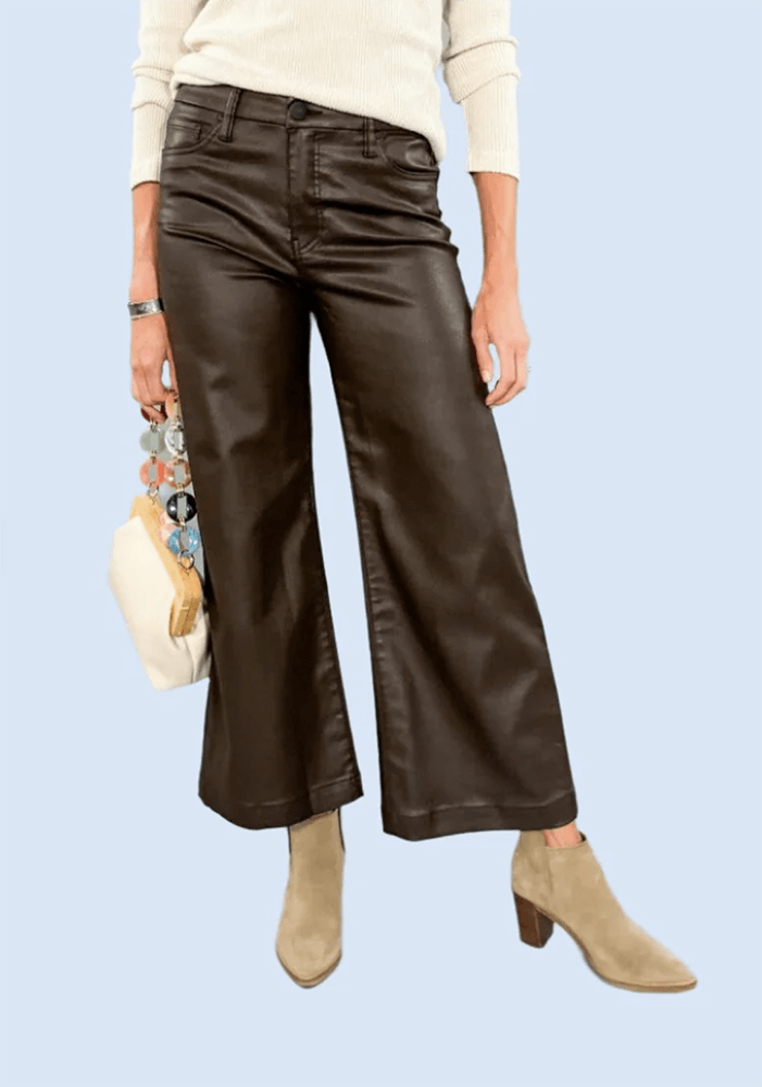 In Birmingham this October, a person is wearing wide-leg dark brown leather pants with a white sweater, light brown ankle boots, and holding a cream-colored handbag with a multi-colored strap. Such chic FINDS make for the perfect autumn ensemble.