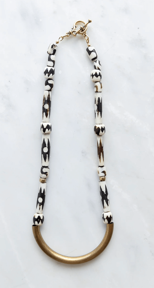 A necklace featuring black and white beads with geometric patterns, and a curved bronze pendant at the bottom, set against a white background. 