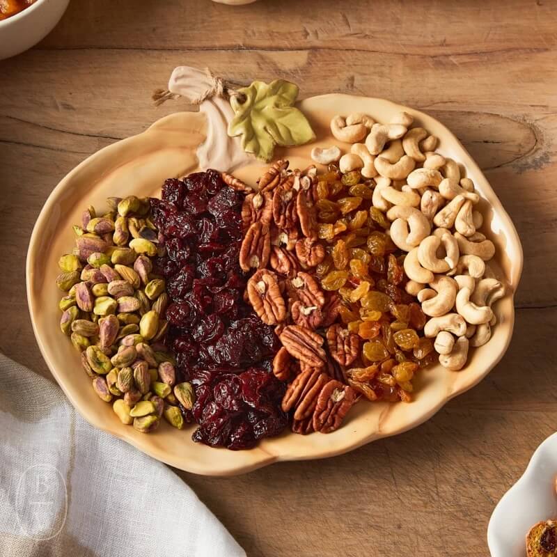 A pumpkin-shaped platter rests on a wooden surface in Memphis, brimming with pistachios, dried cranberries, pecans, raisins, and cashews.