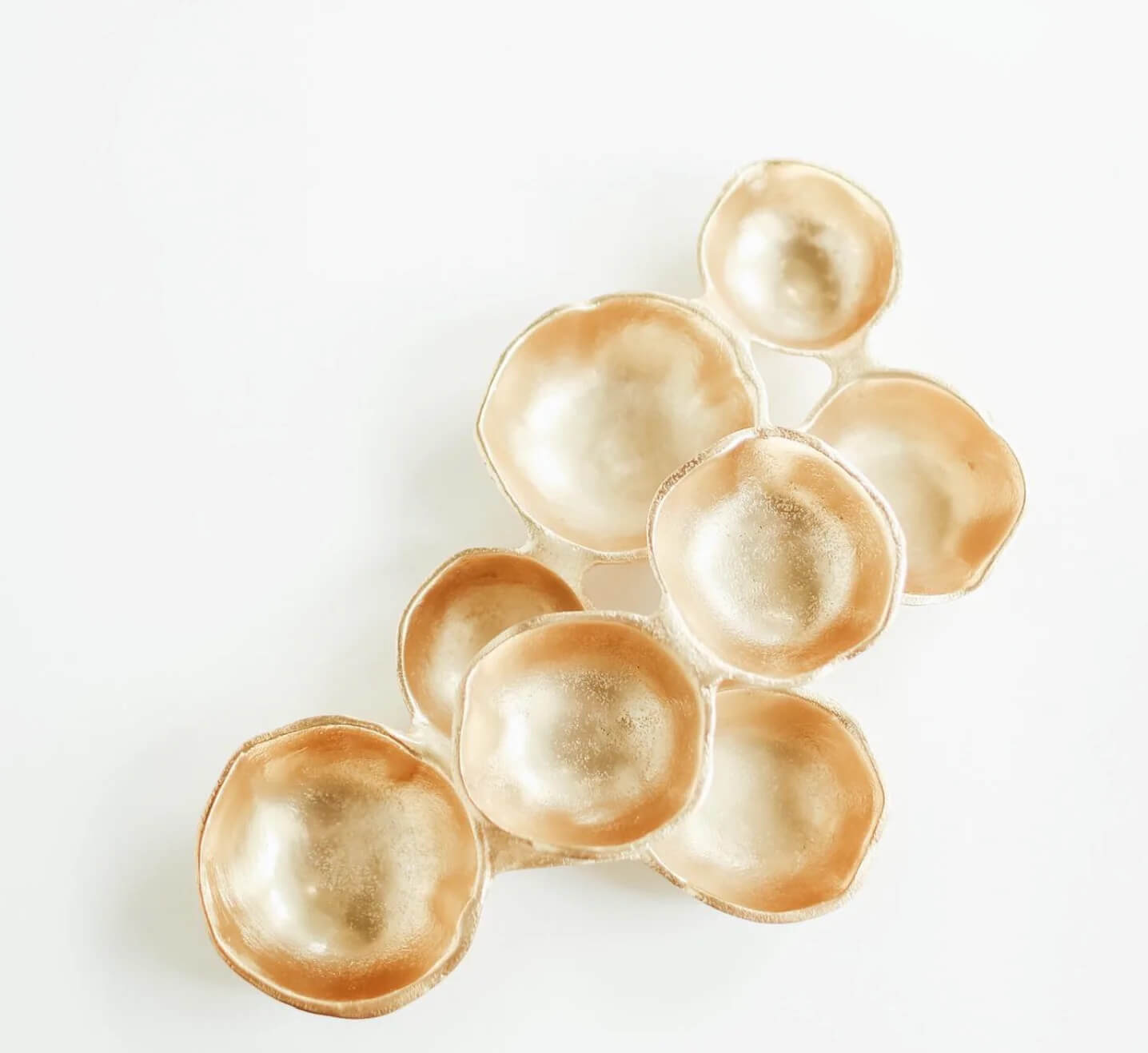 A cluster of round, gold-colored, bowl-like shapes arranged organically on a white background evokes the surprising charm of unexpected FINDS.