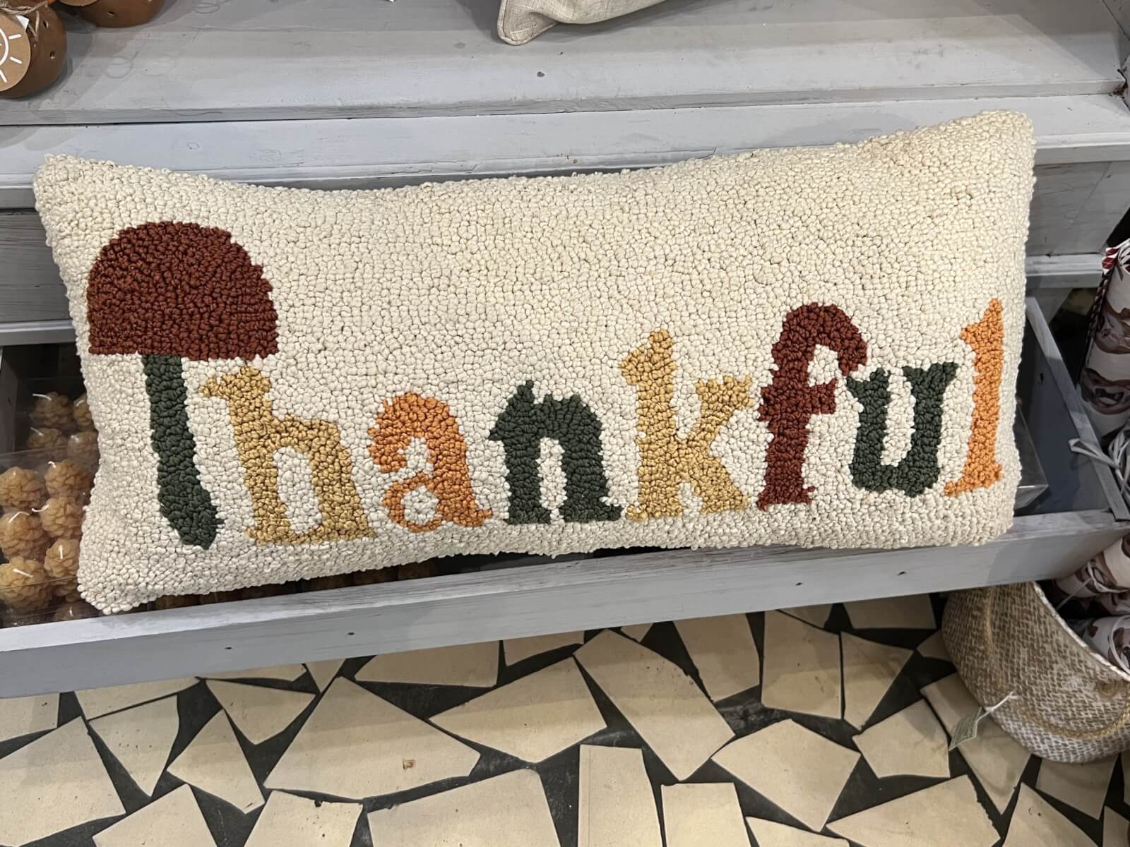 A decorative pillow with textured letters spelling "thankful," featuring an autumn-themed color palette