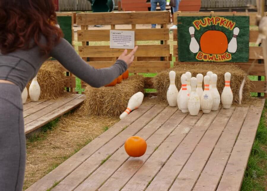 In the heart of Nashville's Pumpkin Patches, a lively game of "Pumpkin Bowling" sets the fall 2024 scene, where a small pumpkin rolls down the wooden lane toward gleaming white pins.