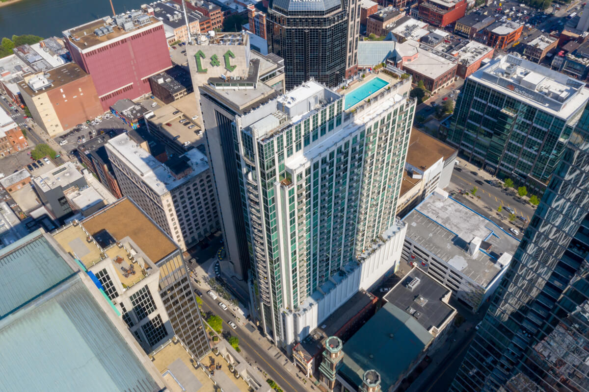 Aerial view of the Nashville cityscape featuring a tall building on 415 Church St with a rooftop pool, surrounded by other buildings and streets.