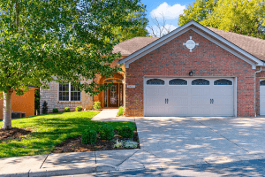 A red brick house on Riva Road, with a two-car garage, surrounded by trees and a well-kept lawn, rests under Louisville KY's clear blue sky.