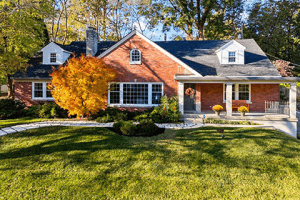 Nestled on Millvale Road in Louisville KY, a red brick house boasts multiple gables, large windows, and a covered porch. It's surrounded by lush green grass and autumnal trees, with a solitary orange tree gracing the front yard.