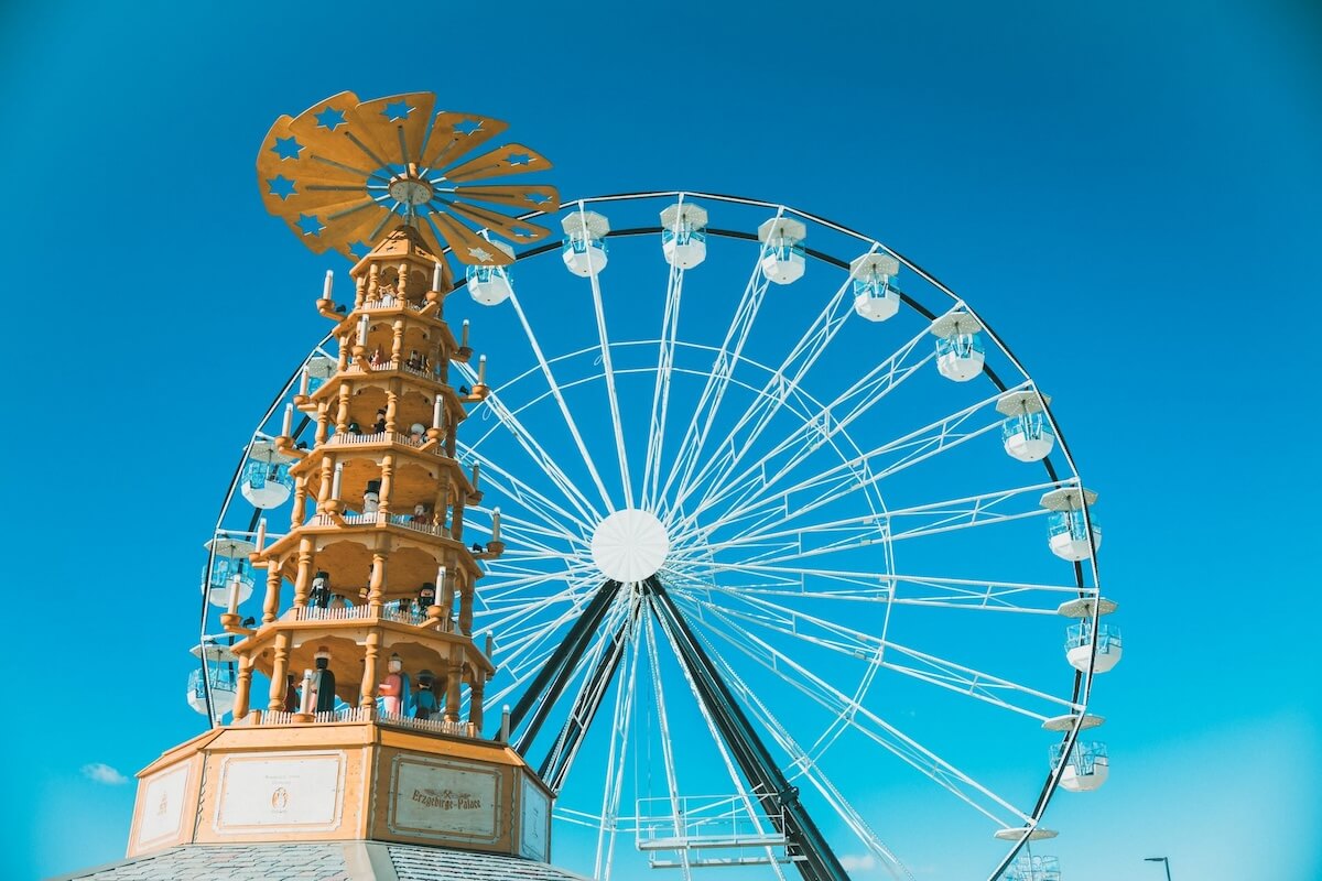 A ferris wheel and a decorative wooden structure with multiple tiers stand against a clear blue sky, reminiscent of the charming attractions found in towns across Alabama.