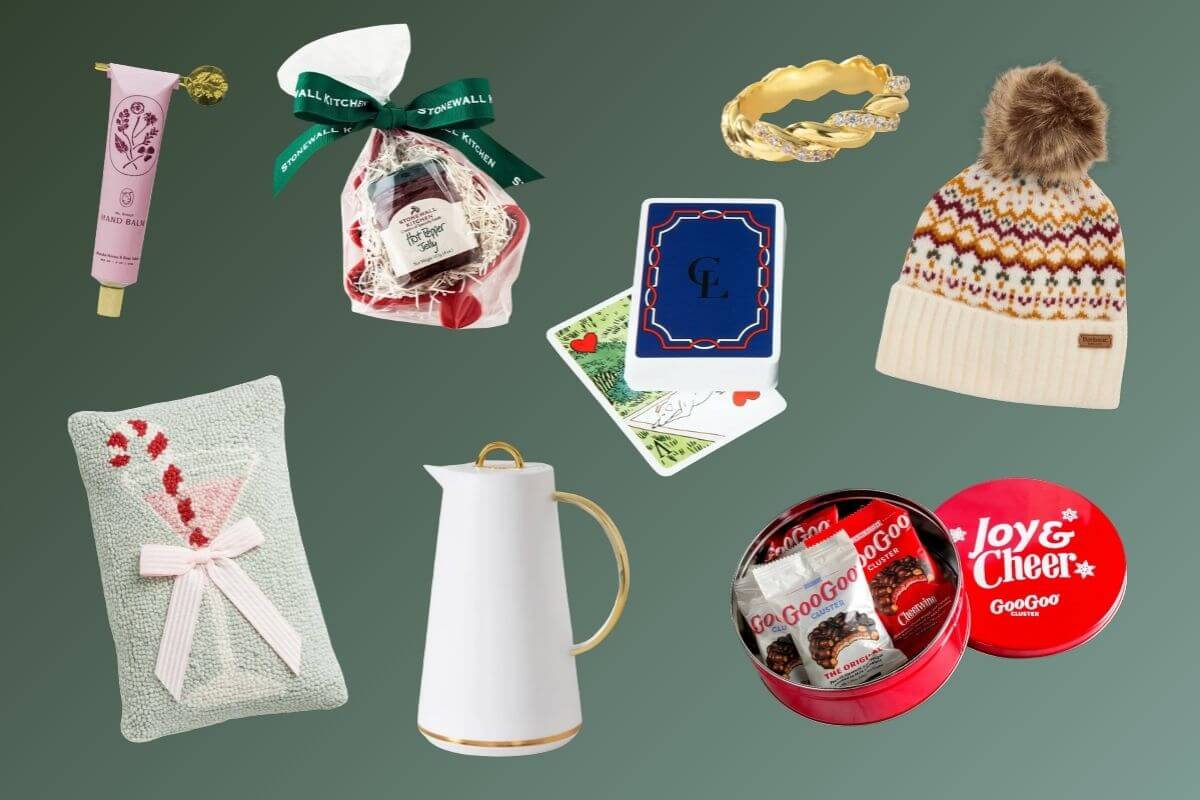 A flat lay of assorted christmas gifts under $50, including a knit hat, hand cream, jam, cards, a gold ring, a white pitcher, chocolates, and a decorative pillow on a green background.