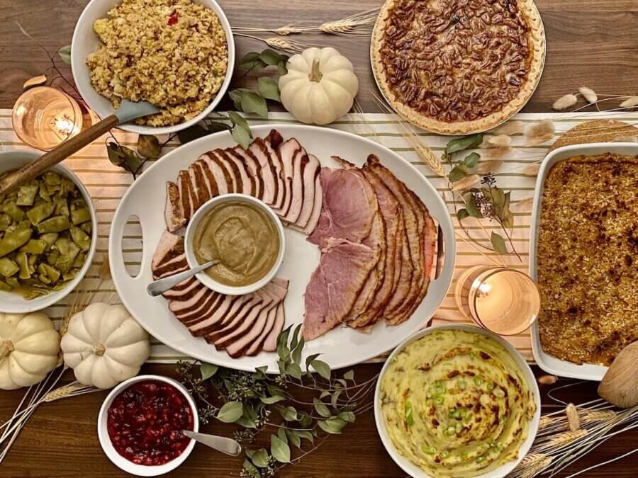 Where to Get Thanksgiving Takeout in Nashville - 2 A Nashville Thanksgiving takeout spread with sliced turkey and ham, gravy, mashed potatoes, green beans, cranberry sauce, stuffing, sweet potato casserole, and pecan pie set on a festively decorated table.