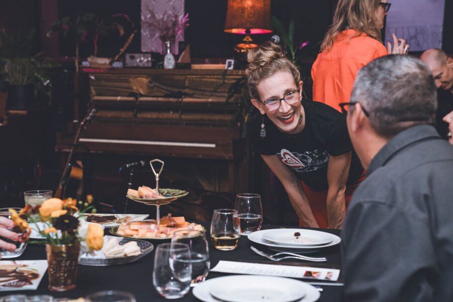 Meet Nashville's Studio Mama, Rebecca Wood - 2 Rebecca Wood leans over the table, engaging guests in conversation at the gathering. The scene is lively, with plates and glasses set neatly, while a piano stands gracefully in the background.