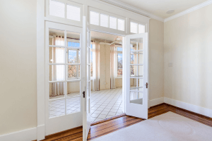 Open French doors lead from a room with wooden flooring to a bright sunroom with tiled flooring and large windows, offering a cozy retreat on Cherokee Road in Louisville, KY.