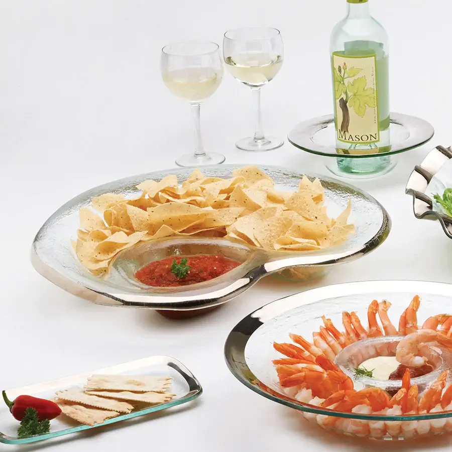 A glass table set with tortilla chips and salsa, shrimp with cocktail sauce, crackers topped with pepper, two glasses of white wine, and a bottle—perfect for those seeking expensive gift ideas for an elegant evening.