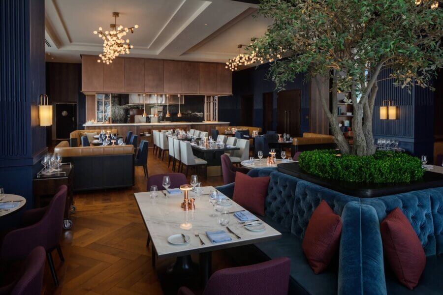 13 Nashville Restaurants OPEN on Christmas Day - 2 Upscale restaurant interior with elegant tables, velvet seating, contemporary lighting, and a large indoor tree centerpiece; open kitchen visible—ideal for those seeking restaurants open on Christmas Day.