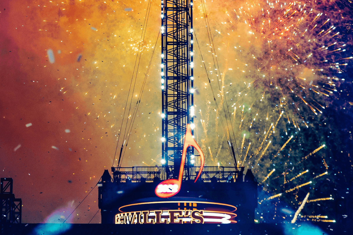 A large neon musical note sign above a building is illuminated as colorful fireworks explode in the night sky, capturing the vibrant energy of New Year's Eve in Nashville.