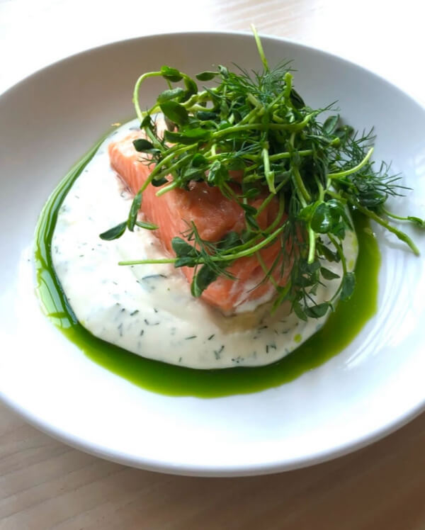 A plate of salmon on creamy dill sauce, topped with fresh greens and served with a drizzle of green oil, is a cherished classic among Nashville restaurants.