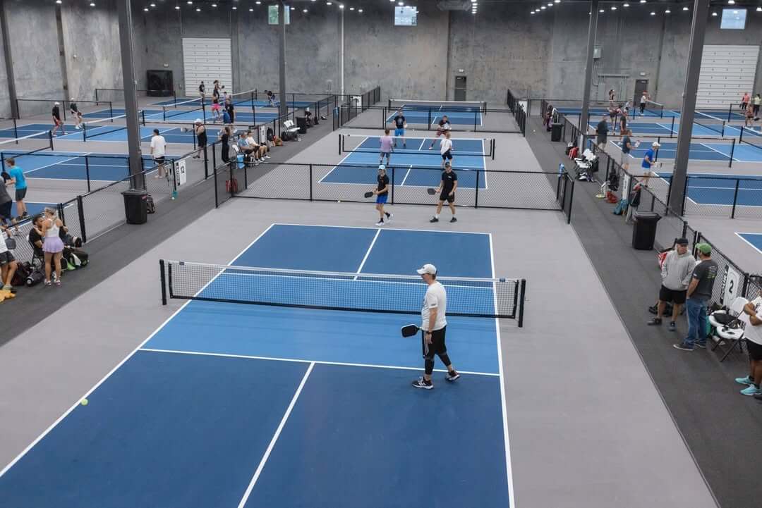 Indoor pickleball courts at the Picklr are buzzing with players engaged in games, surrounded by eager spectators and cozy benches. 