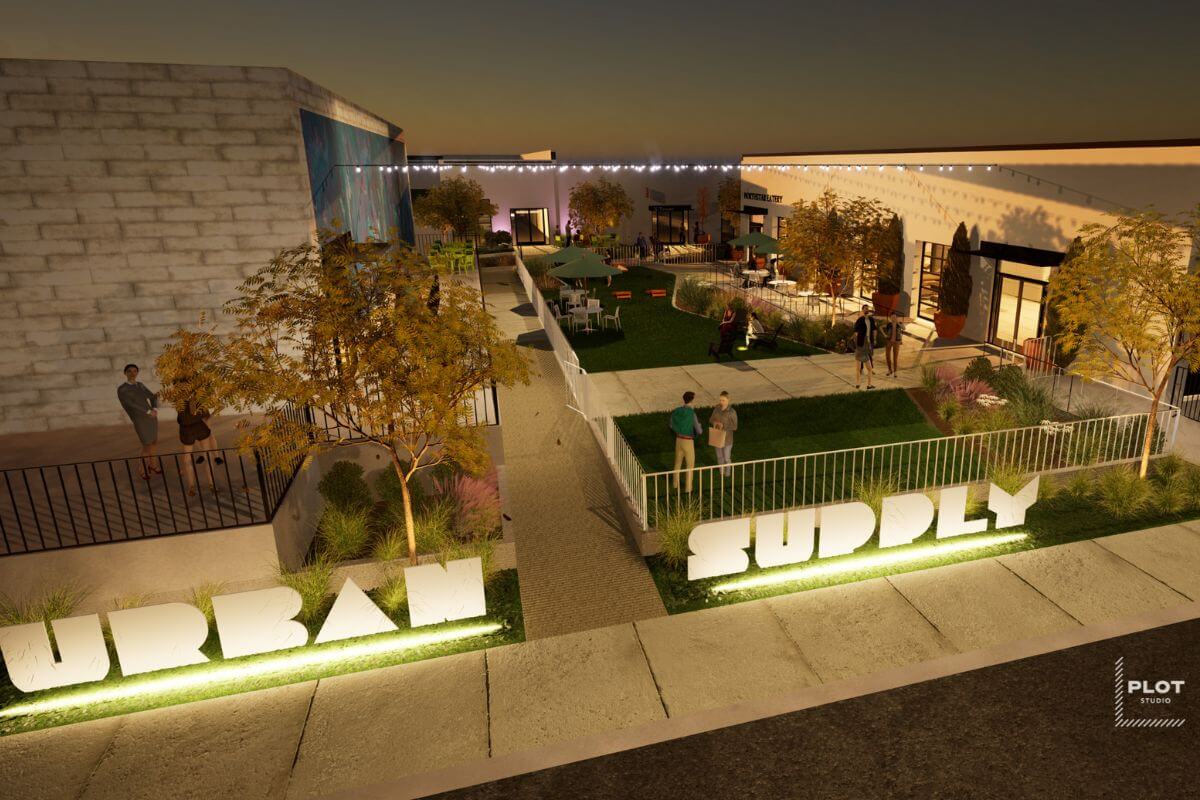 Outdoor urban space at night with grass areas, people, and string lights. Large illuminated signs read "Urban Supply". 