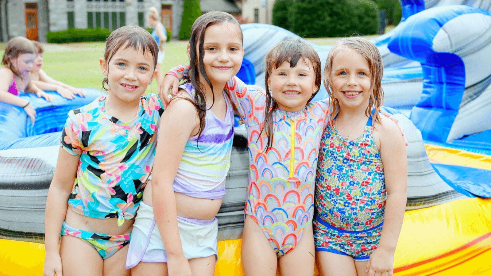 Four children in colorful swimsuits stand smiling in front of an inflatable water slide, capturing the joy and excitement often found at Nashville summer camps.