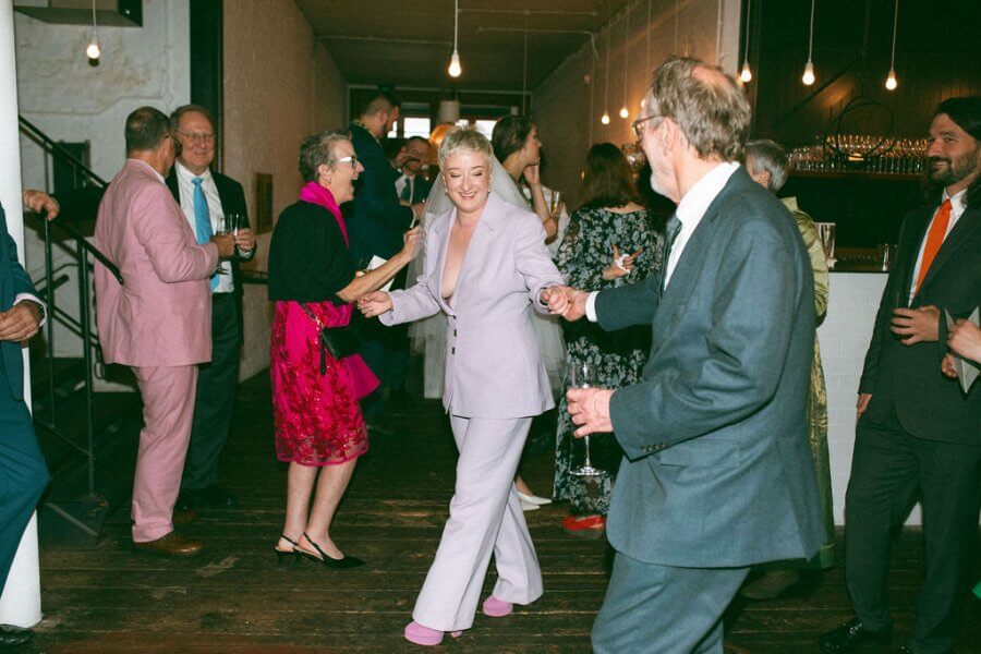 An intimate gathering unfolds as people in formal attire dance gracefully on the wooden floors, bathed in the glow of hanging lights. Amidst whispers and laughter, some guests mingle in the background, adding to the charm of this elegant event in Edinburgh.